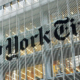 Exterior of The New York Times building at night, with illuminated windows and the newspaper's name visible on the facade