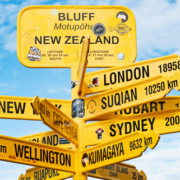 Multiple directional signs in New Zealand pointing toward international destinations including London, Sydney, Wellington, New York, Suqian, and Kumagaya