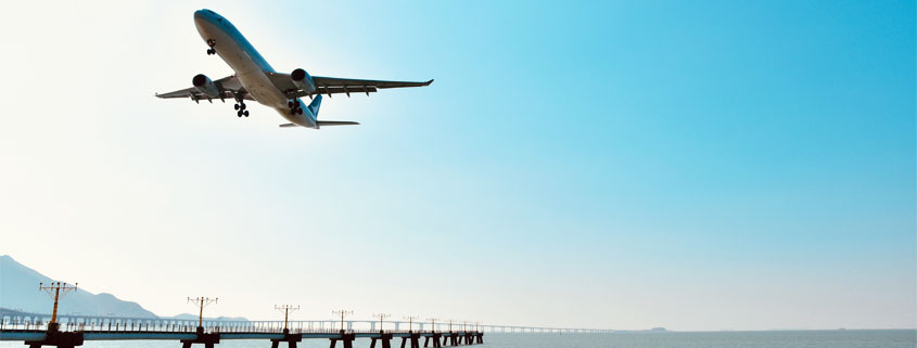Passenger airplane descending toward a coastal airport runway while flying low over the ocean