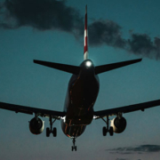 Passenger airplane descending toward an airport with its landing gear extended against the fading evening sky