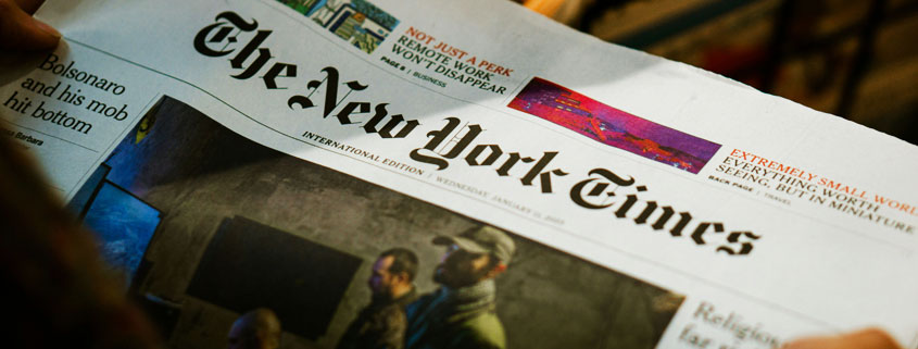 Person reading a printed edition of The New York Times newspaper, reflecting traditional journalism and the experience of following current events