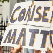 Hands holding a sign reading Consent Matters during a public protest rally