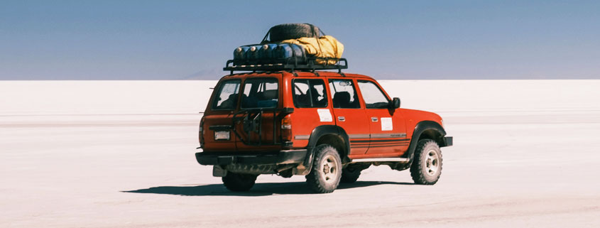 Red-Toyota-Truck-Traveling-Across-Salar-de-Uyuni-Salt-Flats-Bolivia Red Toyota truck on the Salar de Uyuni salt flats in Bolivia with travel equipment secured to its roof