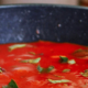 Rich red tomato sauce topped with fresh green herbs in a cooking pan, showing the color and texture of the prepared sauce