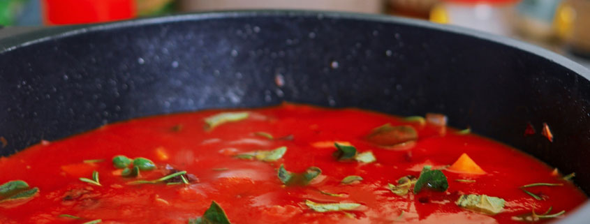 Rich red tomato sauce topped with fresh green herbs in a cooking pan, showing the color and texture of the prepared sauce