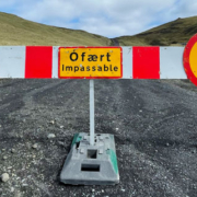 Unpaved countryside road running between two open fields with a road closure sign positioned in the center indicating that the route is impassable