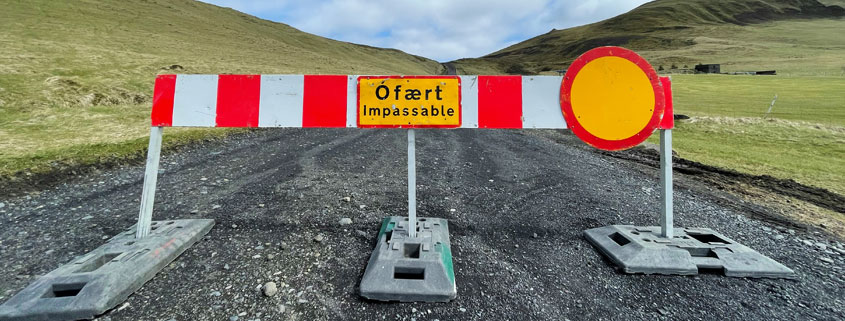 Rural-Countryside-Road-Closed-With-Impassable-Sign Unpaved countryside road running between two open fields with a road closure sign positioned in the center indicating that the route is impassable
