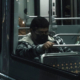 Passenger appearing to sleep in his seat aboard a night train, visible through an illuminated carriage window