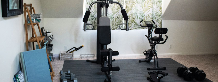 Small-Home-Gym-With-Exercise-Machine-and-Workout-Weights Compact home gym featuring an exercise machine and workout weights arranged in a small indoor fitness space
