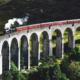Steam train crossing the historic Glenfinnan Viaduct surrounded by the mountainous landscape of the Scottish Highlands