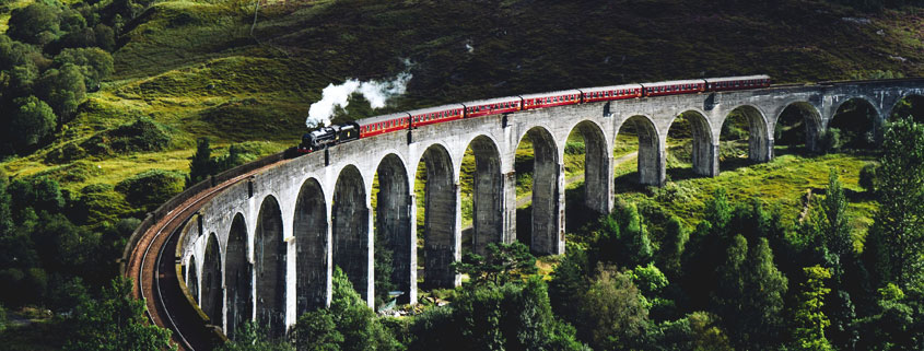 Steam-Train-Crossing-Glenfinnan-Viaduct-Scottish-Highlands Steam train crossing the historic Glenfinnan Viaduct surrounded by the mountainous landscape of the Scottish Highlands