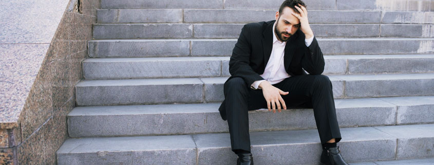 Stressed-Businessman-Sitting-on-Outdoor-Stairs-Contemplating-Work-Problems Upset young businessman sitting alone on outdoor stairs, appearing stressed and overwhelmed by work-related problems