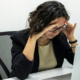 Tired young female employee experiencing stress and a headache while working at a computer