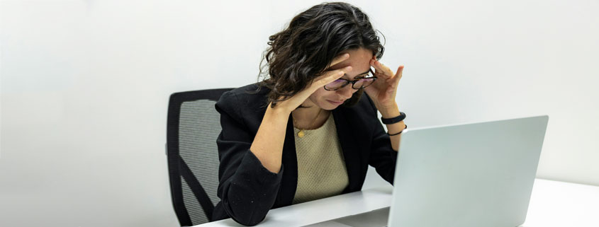 Tired young female employee experiencing stress and a headache while working at a computer