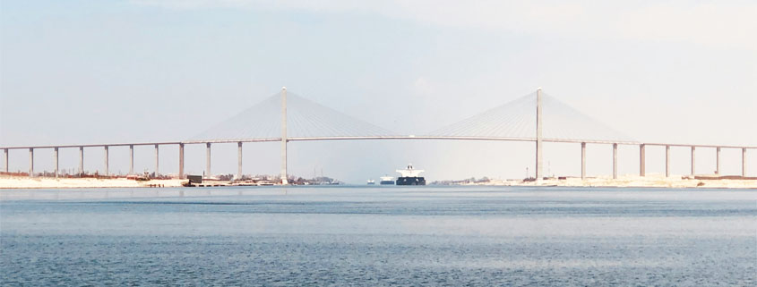 Cargo ship approaching the Suez Canal suspension bridge in Egypt, with the vessel visible in the distance along the waterway