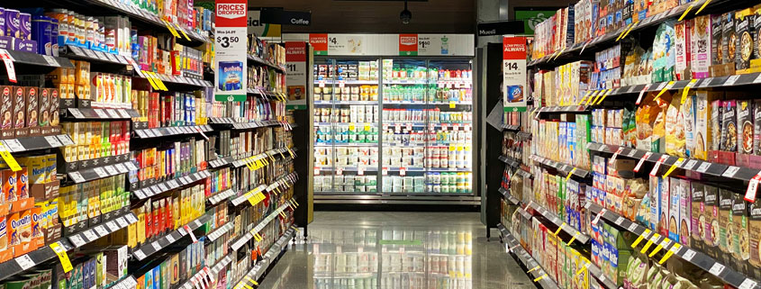 Supermarket-Aisle-With-Packaged-Foods-and-Dairy-Products Supermarket aisle displaying a variety of food products including cheese, dairy items, candy, cookies, and biscuits