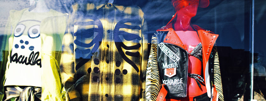 Three mannequins dressed in different fashionable outfits displayed together in a clothing store window