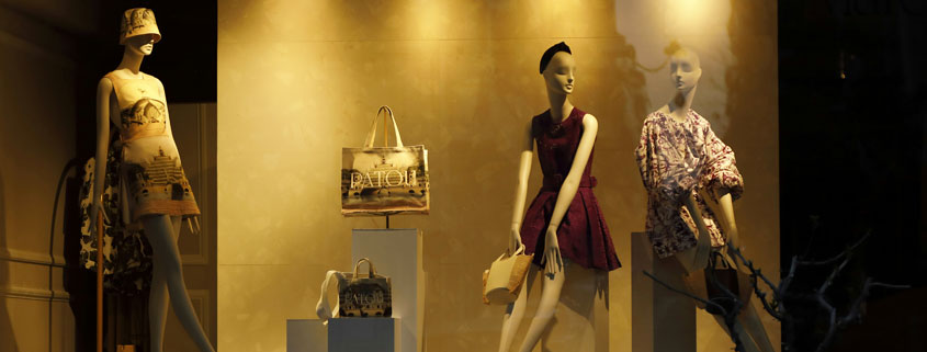 Three mannequins wearing different fashionable outfits and dresses, arranged in standing and seated positions
