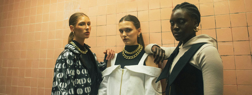 Three-Women-Different-Fashion-Styles-Beauty-and-Body-Image Three women wearing different fashionable outfits standing closely together, with the women on either side resting their arms on the shoulders of the woman in the center