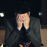 Tired young businessman wearing a suit and tie working late at night, typing on a computer in a dark office