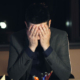 Tired young businessman wearing a suit and tie working late at night, typing on a computer in a dark office