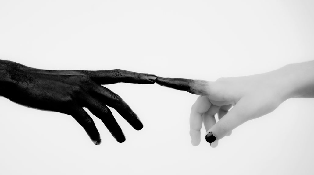 Two-Contrasting-Hands-Touching-Fingertips-in-Connection Close-up of two contrasting hands gently touching fingertips, one entirely black and the other light-colored with a black-painted fingertip and thumbnail, symbolizing connection and communication