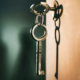 Two metal keys connected by a keychain, with one key inserted into a door lock and the other hanging below
