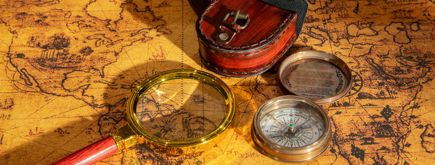 Vintage-Map-With-Antique-Compass-and-Magnifying-Glass Vintage geographical map with an antique compass and handheld magnifying glass for examining locations and routes