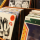 Rows of music albums with colorful covers arranged in wooden display bins along an aisle inside a record store