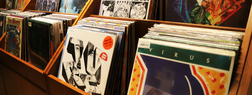 Rows of music albums with colorful covers arranged in wooden display bins along an aisle inside a record store