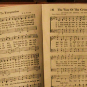 Open hymn book resting on an old piano displaying sheet music for Yield Not to Temptation and The Way of the Cross Leads Home