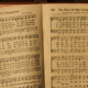 Open hymn book resting on an old piano displaying sheet music for Yield Not to Temptation and The Way of the Cross Leads Home