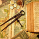 Vintage map surrounded by an antique compass, old book, dollar bill, bullet, and travel postcards depicting traditional destinations around the world