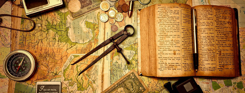 Vintage map surrounded by an antique compass, old book, dollar bill, bullet, and travel postcards depicting traditional destinations around the world