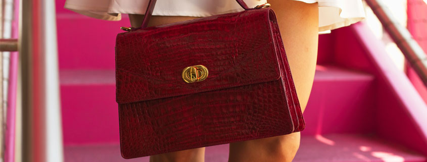 Woman-Carrying-Fashion-Handbag-Beside-Her-Legs Fashion handbag hanging beside a woman's legs, with the lower portion of her skirt visible as she stands