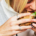 Woman eating a burger or sandwich with a smoothie-style drink beside her, illustrating everyday eating habits and food consumption