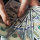 Woman's hands holding and spreading several US hundred-dollar bills in a fan-shaped arrangement