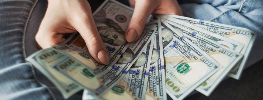 Woman's hands holding and spreading several US hundred-dollar bills in a fan-shaped arrangement