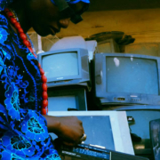 Black woman holding a vintage cassette radio with a collection of old-fashioned television sets displayed behind her