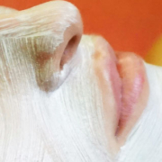 Woman lying down during a skincare treatment with a white facial mask covering her forehead, cheeks, and nose while leaving her eyes and lips uncovered
