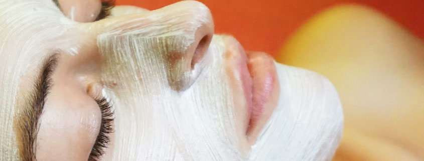 Woman lying down during a skincare treatment with a white facial mask covering her forehead, cheeks, and nose while leaving her eyes and lips uncovered