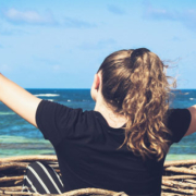 Woman sitting in a round woven basket boat near the shoreline with both arms raised in the air