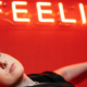 Woman lying comfortably on a sofa with her eyes open and one hand visible beneath a sign displaying the word Feelings