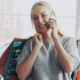 Smiling blonde woman carrying shopping bags and talking on her mobile phone while browsing clothing racks in a large fashion store