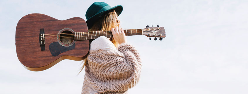 Woman-Walking-With-Guitar-on-Shoulder-and-Green-Hat.jpg