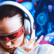 Woman wearing futuristic wraparound cyber glasses and headphones, holding both sides of her headphones while looking downward and concentrating on music