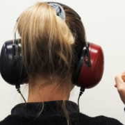 Woman viewed from behind wearing headphones and raising her index finger to indicate hearing a sound during a hearing test