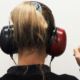 Woman viewed from behind wearing headphones and raising her index finger to indicate hearing a sound during a hearing test
