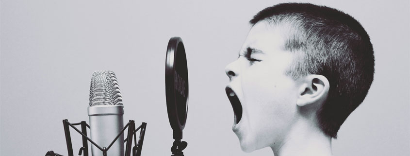 Young boy with his mouth wide open in front of a recording microphone, appearing to sing or shout