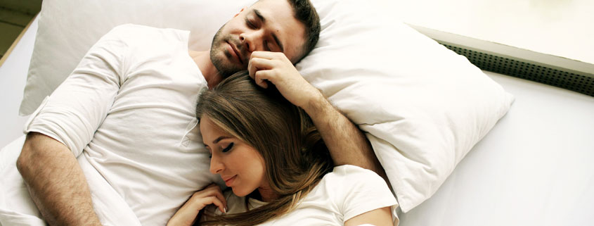 Young-Couple-Kissing-and-Embracing-in-Bed-After-Waking-Up Young couple sharing a kiss and affectionate embrace while waking up together in bed in the morning